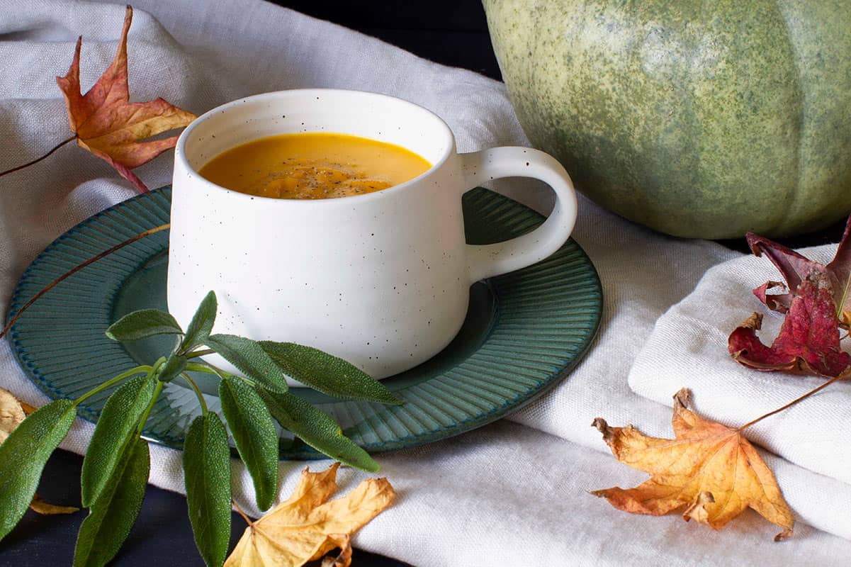 A white cup of pumpkin soup on a green plate, cosy scene.