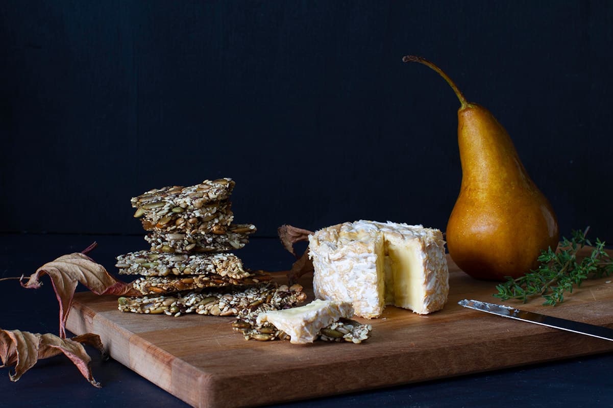 Five Seed Crackers A stack of five seed crackers, brie and pear on a wooden board.