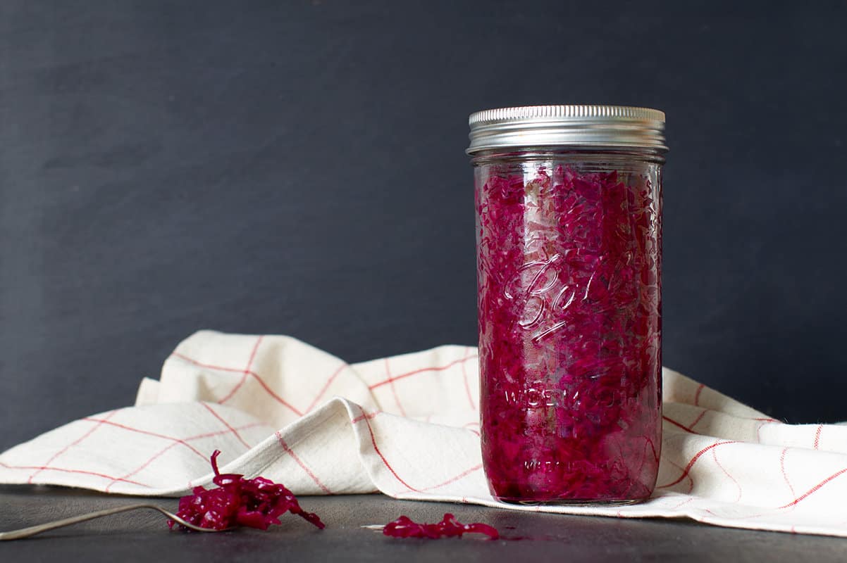 A glass of red sauerkraut in front of a tea towel, dark background