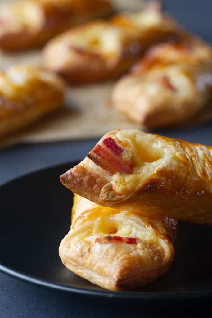 Two zoomed in cheese and bacon turnovers on a black plate