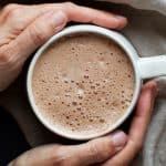 Hot chocolate in a white cup held by two hands.