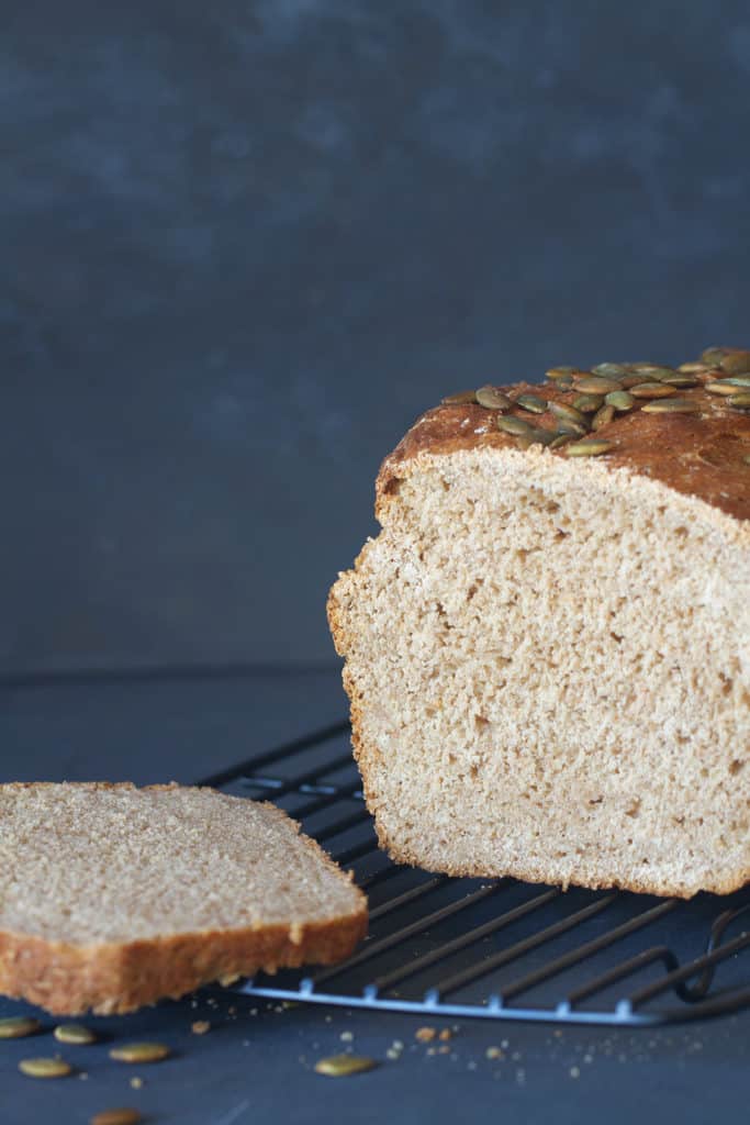 A loaf and slice of soft whey bread on a black cooling rack. Dark background.