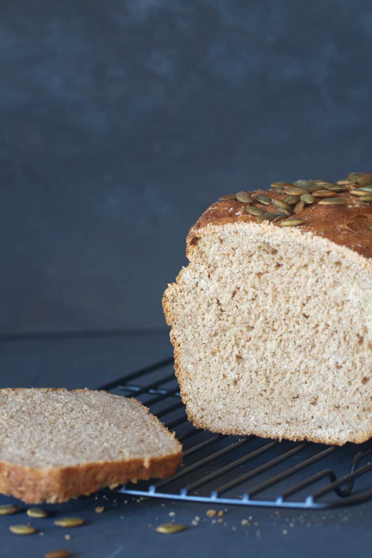 A loaf and slice of soft whey bread on a black cooling rack. Dark background.