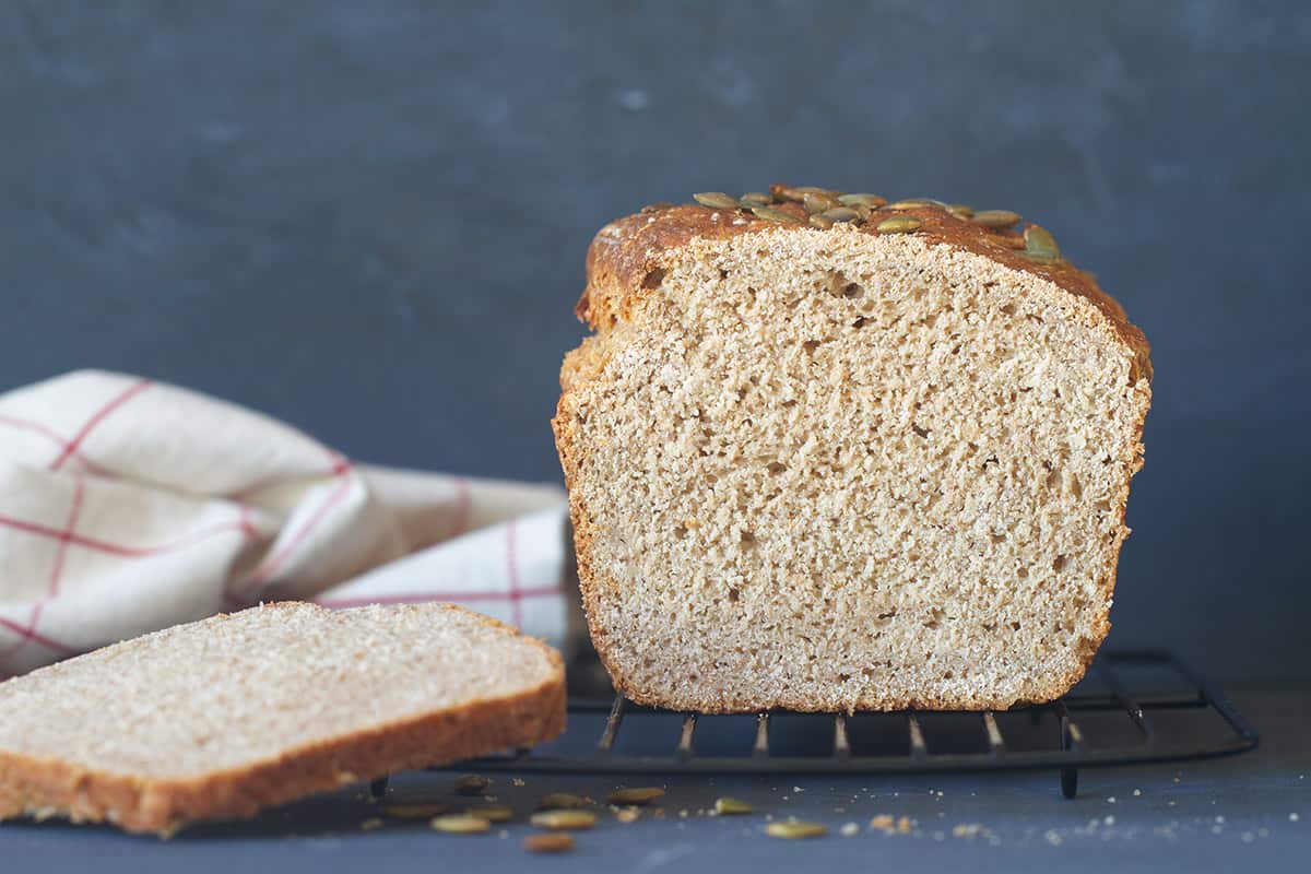 A loaf and slice of soft whey bread on a black cooling rack. Dark background.