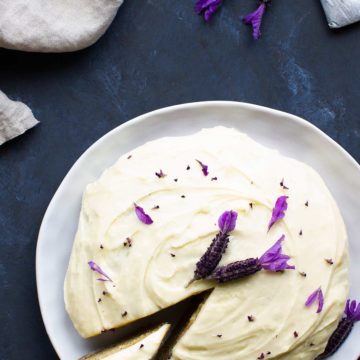Bird's eye view of an earl grey lavender cake on a white plate next to lavender, a teabag and a linen tea towel.