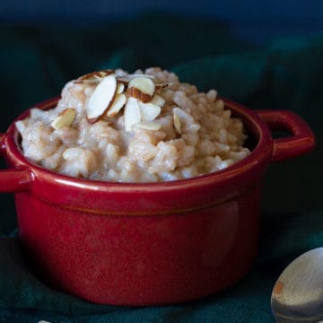 A red bowl of creamy rice pudding on a dark background.