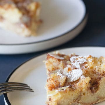 A slice of sourdough bread pudding on a white plate. Another plate is blurred out in the background.