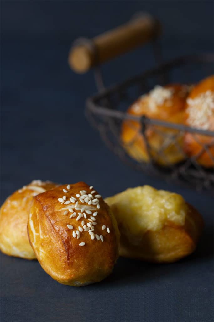 Three pretzel bites with different toppings. A basket of more bites is in the background blurred out.