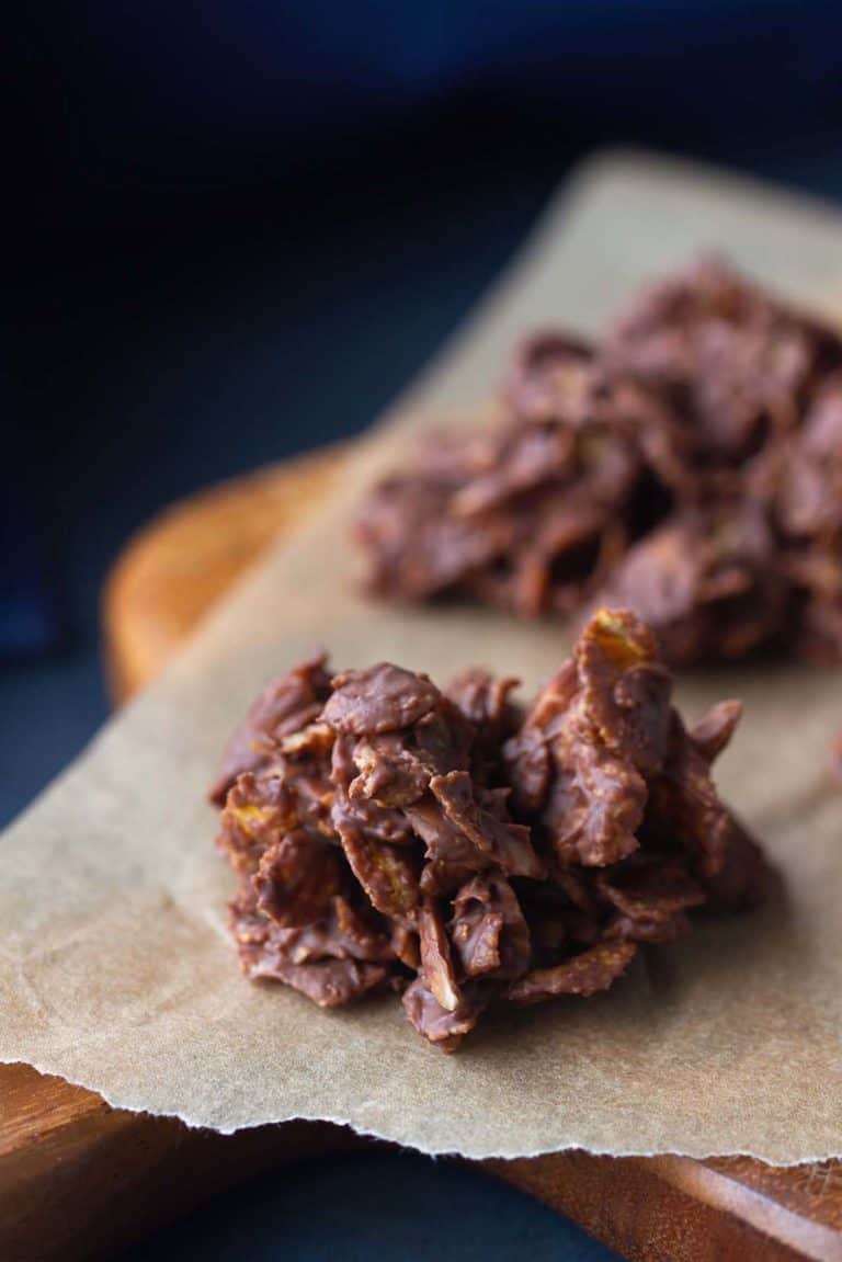 Chocolate crossies (aka Schokocrossies) on baking paper and a wooden board. Moody scene.