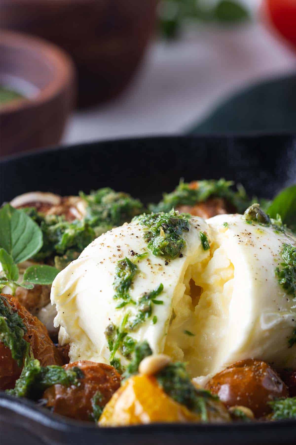 Close-up of a ball of burrata covered with salsa verde and next to slow-roasted tomatoes.