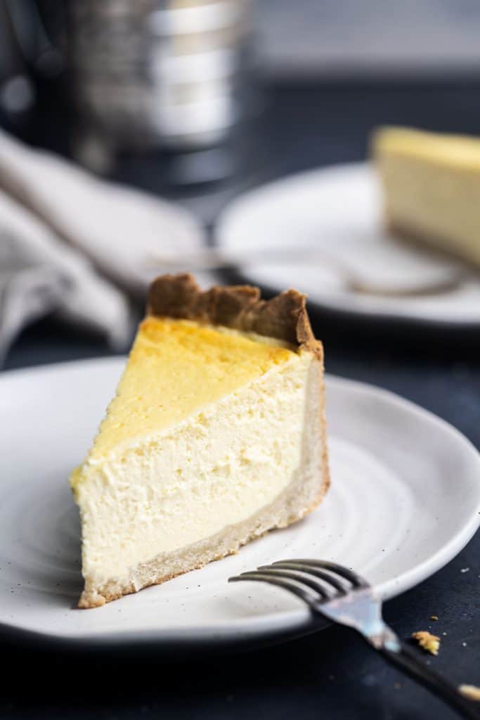 A slice of Rahmkuchen on a plate with a fork. Another slice is in the background blurred out.
