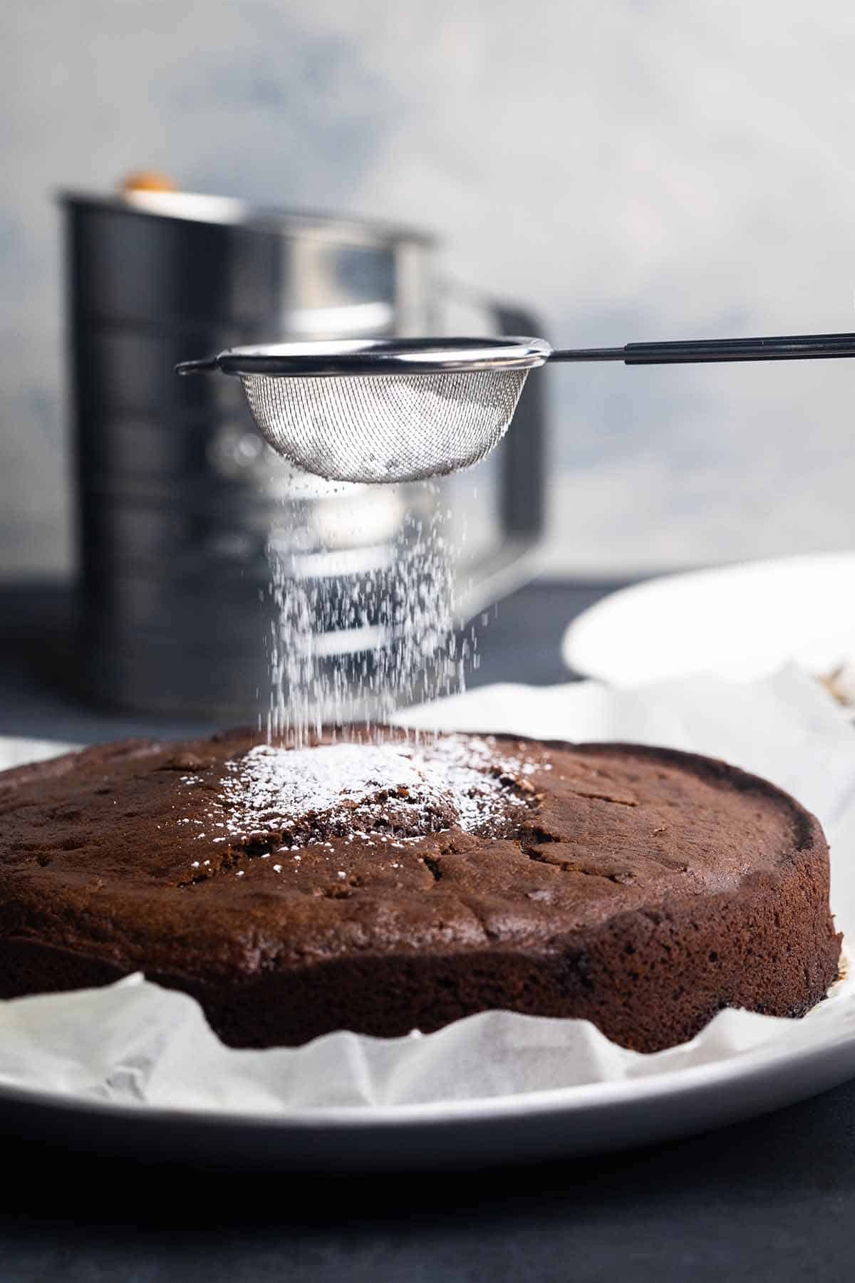 A German chocolate cake on a white plate. Powdered sugar is being added.