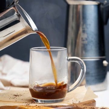 A Moka pot pouring coffee into a glass cup.