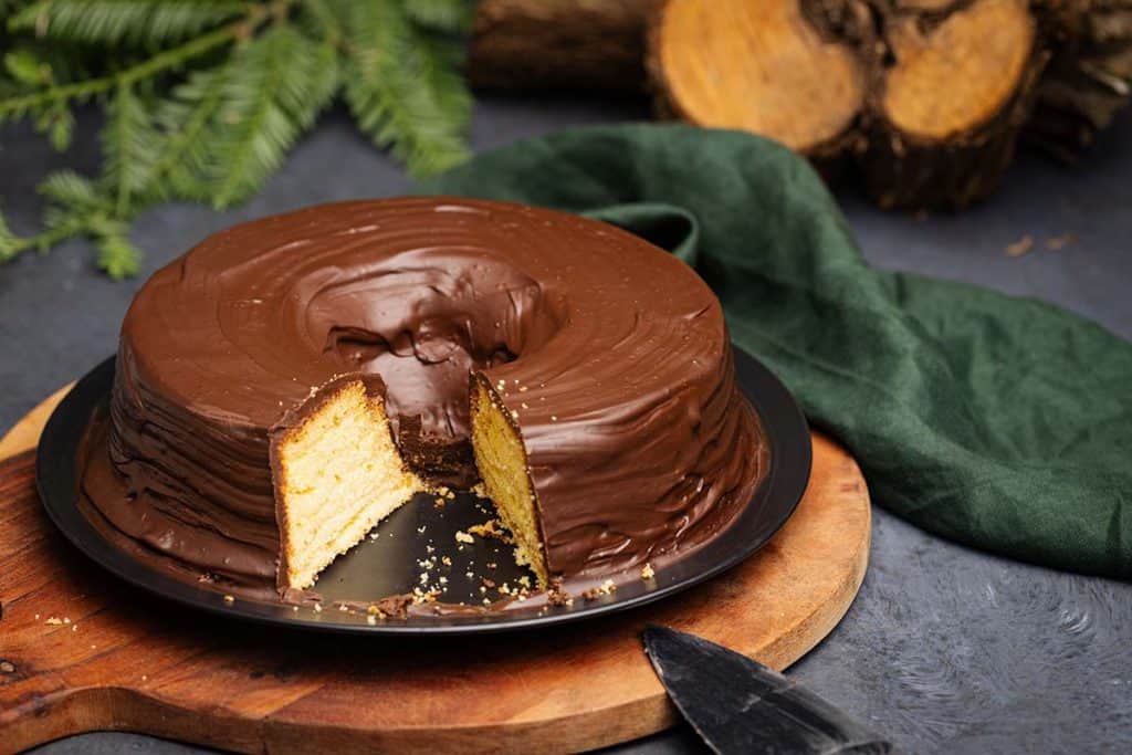 Baumkuchen on a wooden board next to a log and foliage.