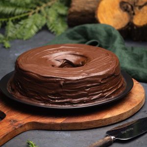 Baumkuchen on a wooden board next to a log and foliage.