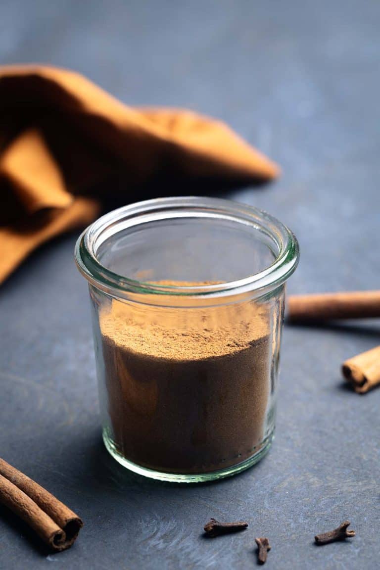 A jar of Christmas spice mix in a moody setting next to cinnamon quills.