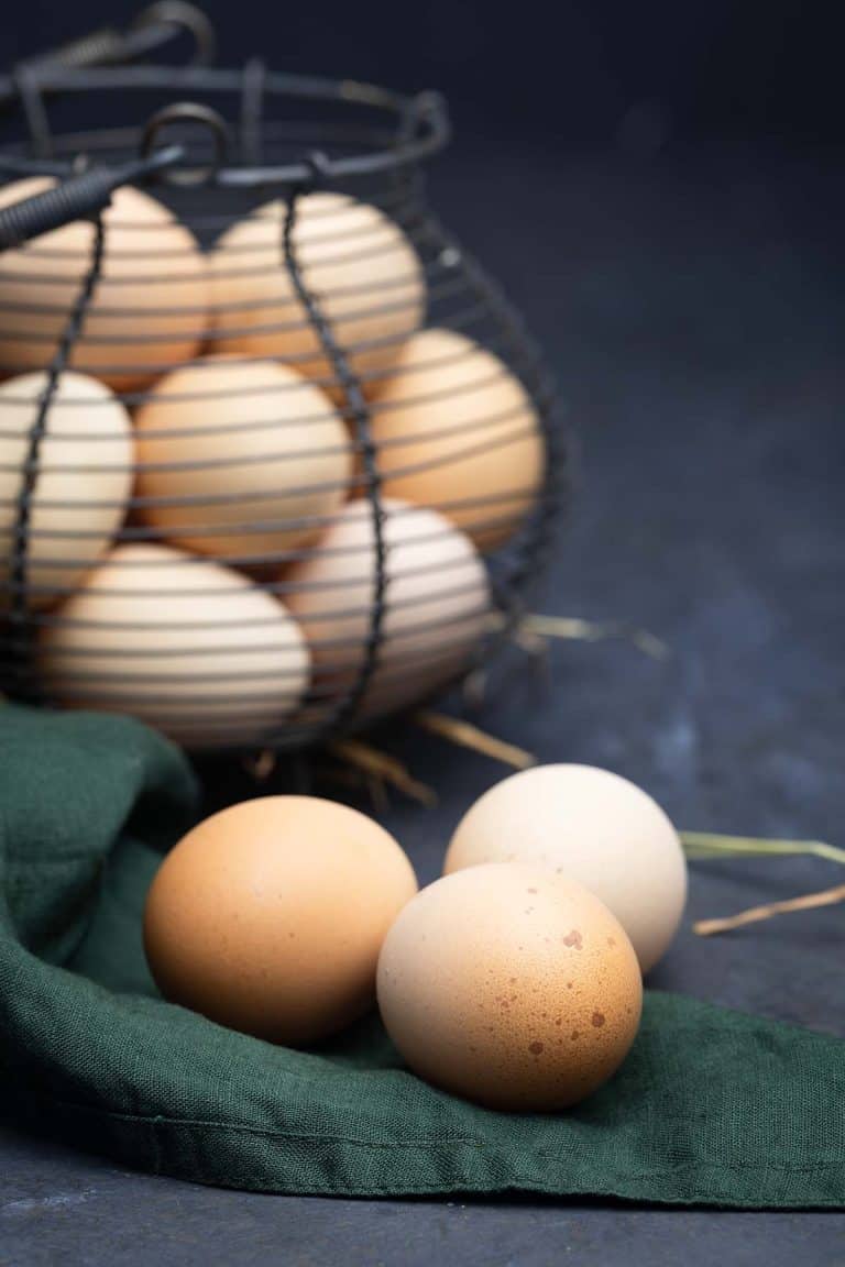 Three farm fresh eggs on a green napkin. Egg basket behind.