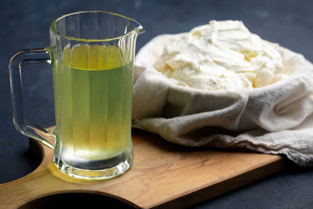 A jug of leftover liquid whey next to yogurt.