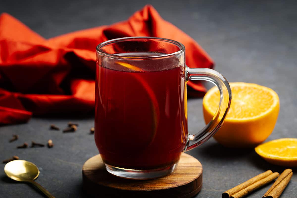 A glass cup filled with winter spiced tea next to spices. Moody setting.