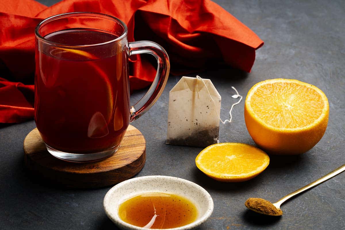 A glass cup filled with winter spiced tea next to spices. Moody setting.