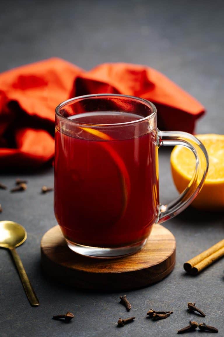 A glass cup filled with winter spiced tea next to spices. Moody setting.