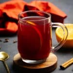 A glass cup filled with winter spiced tea next to spices. Moody setting.