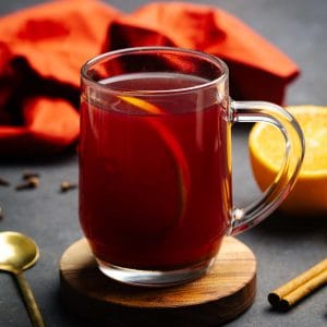 A glass cup filled with winter spiced tea next to spices. Moody setting.