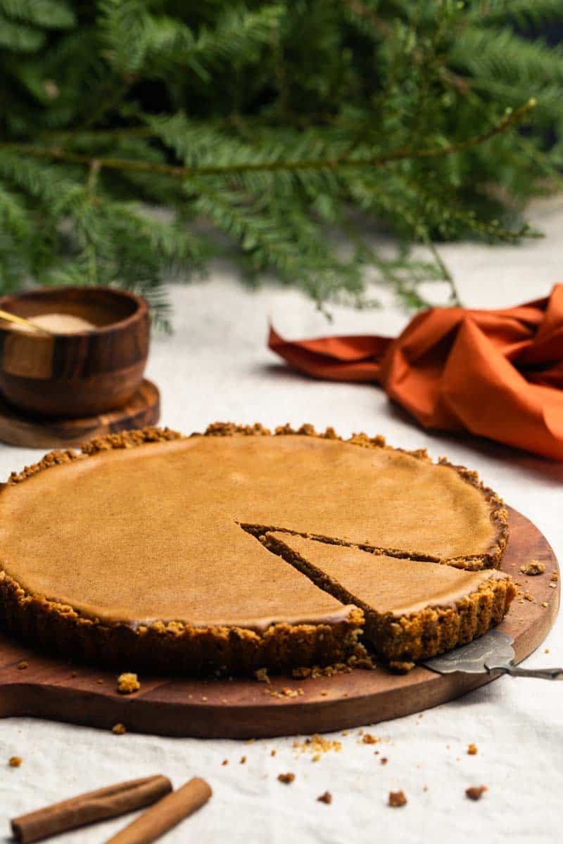 A slice being taken out of a cinnamon pie with pretzel crust. Fall-colored, cozy scene.