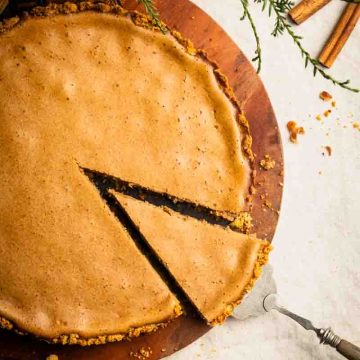A slice being taken out of a cinnamon pie with pretzel crust. Fall-colored, cozy scene.