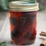 A glass of cinnamon quill extract next to cinnamon quills.