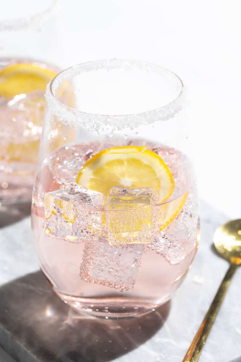 Two Rosé lemonade cocktails on a marble tray next to a golden spoon.