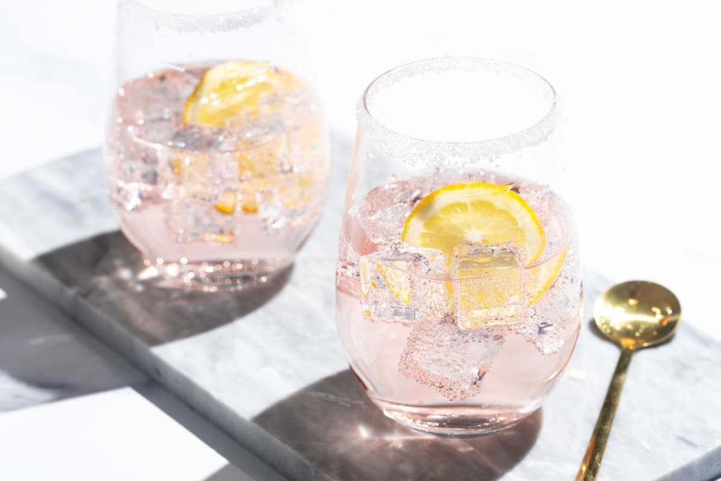 Two Rosé lemonade cocktails on a marble tray next to a golden spoon.