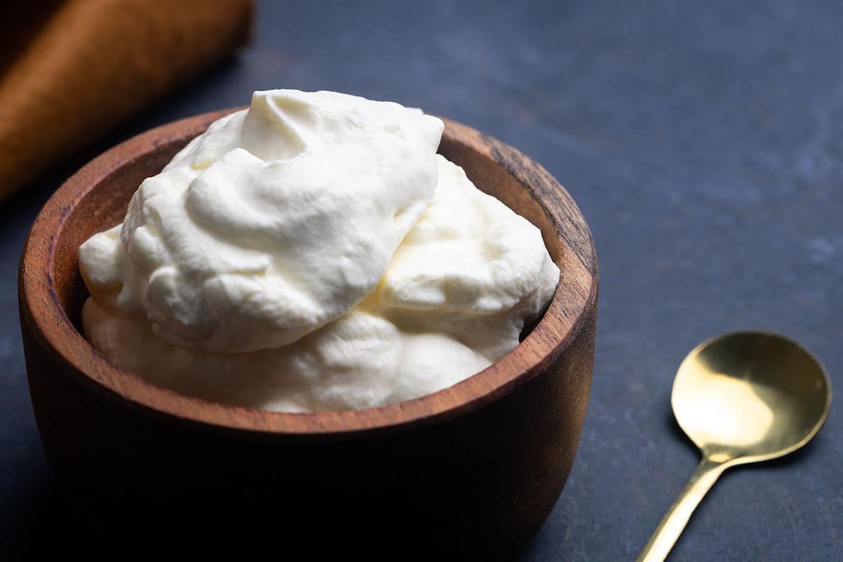 A wooden bowl filled with schlag next to a golden spoon and napkin.