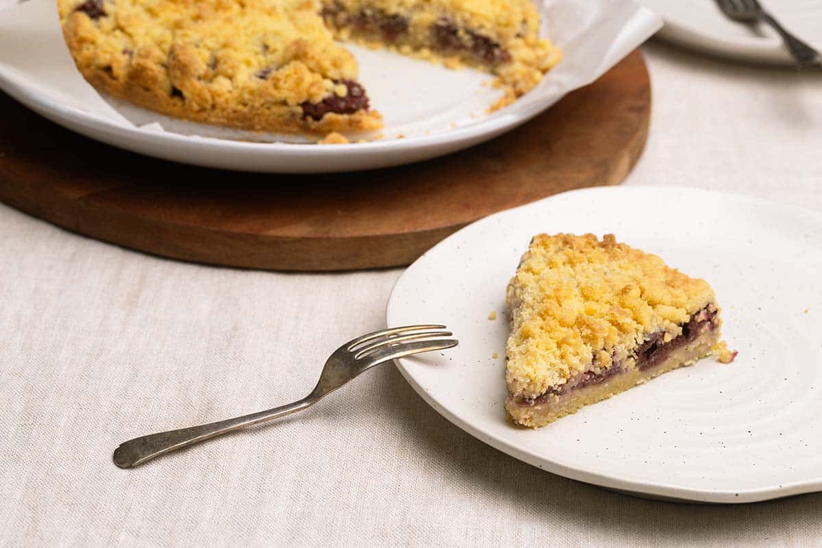 A piece of Streuselkuchen on a plate next to a whole German crumb cake.