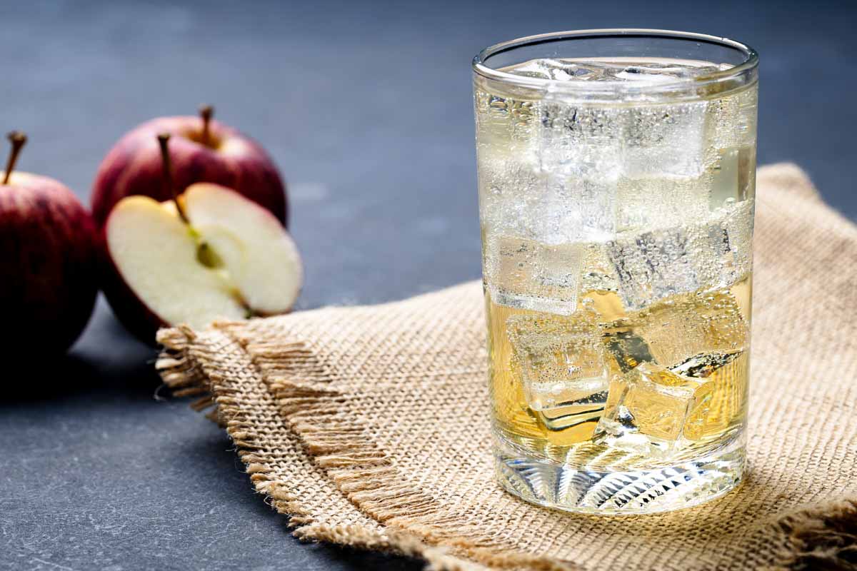 A glass of Apfelschorle on hessian fabric next to apples.