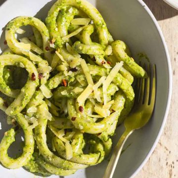 A bowl of pici pasta with creamy lemon pesto sauce next to a linen tea towel.