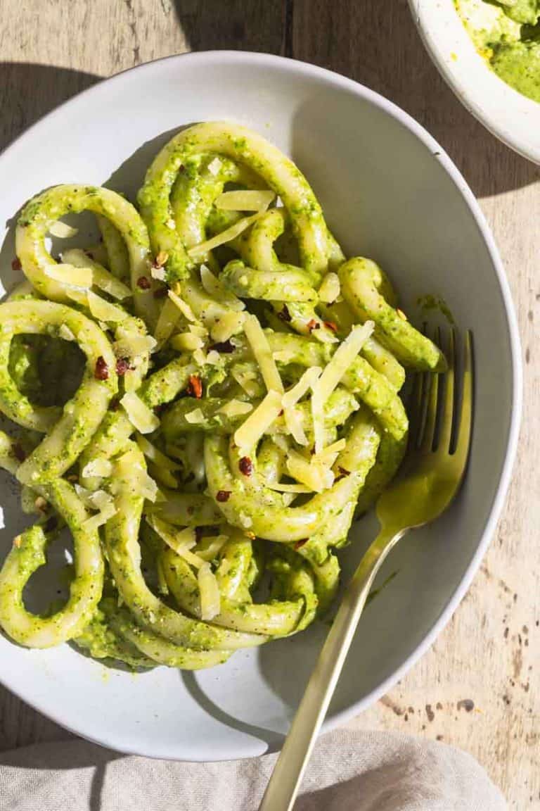 A bowl of pici pasta with creamy lemon pesto sauce next to a linen tea towel.
