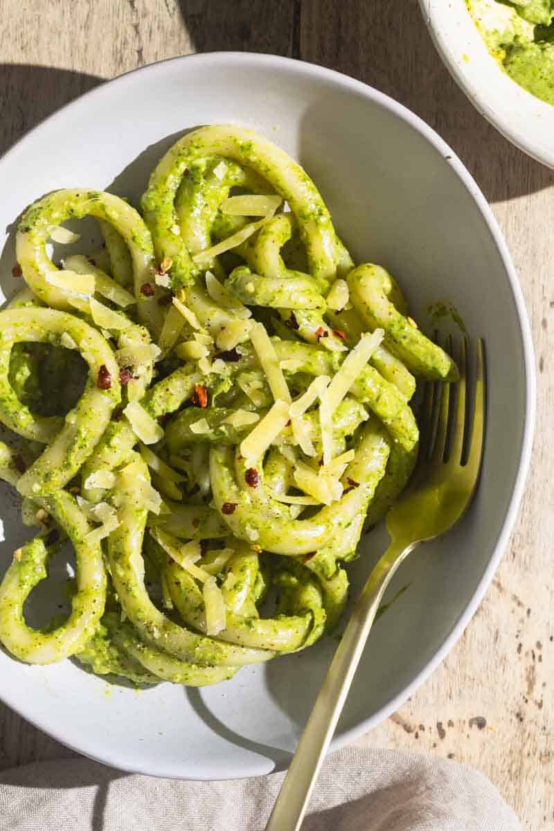 A bowl of pici pasta with creamy lemon pesto sauce next to a linen tea towel.