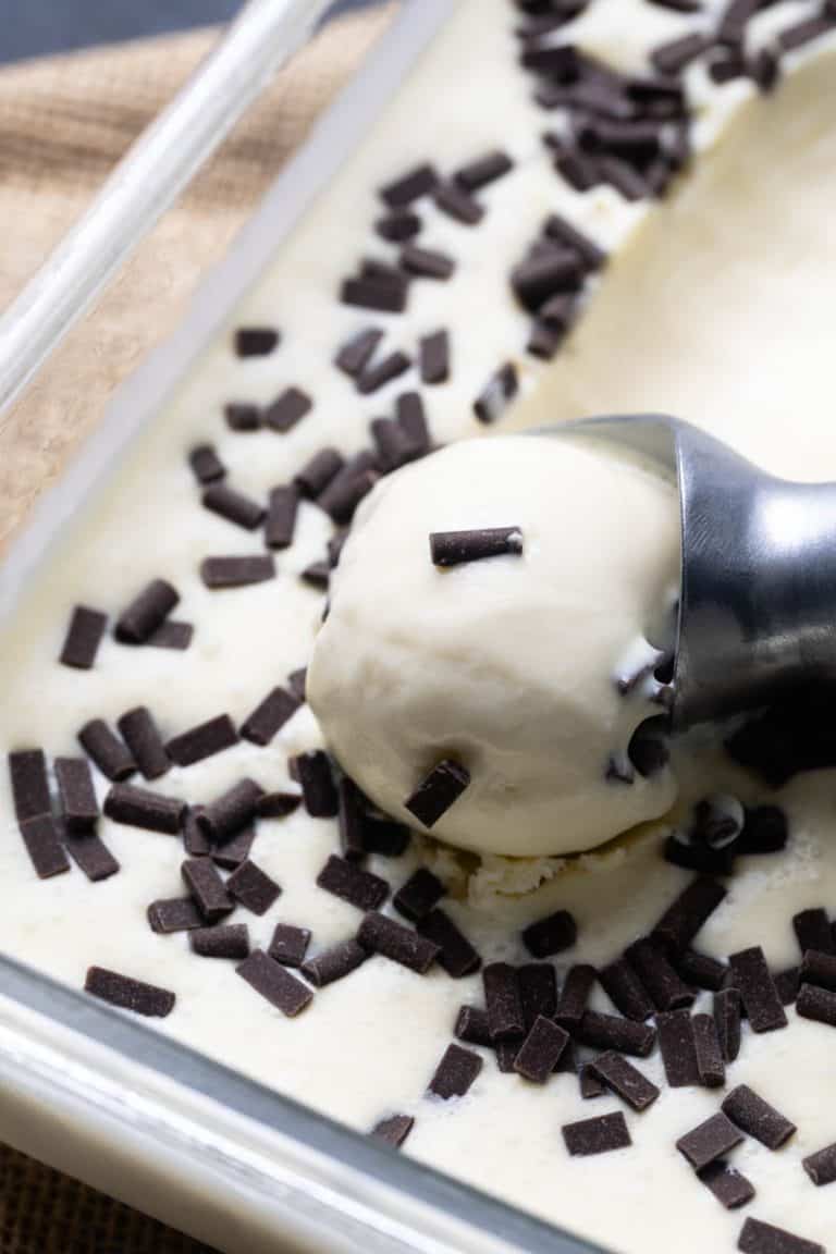 Stracciatella ice cream in a glass container. A portion is being scooped.