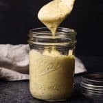 A jar of homemade dijonnaise. A spoon is taking a serving.
