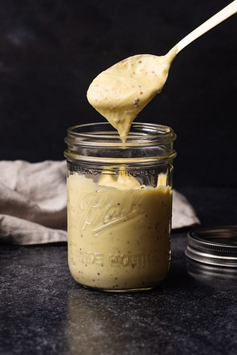 A jar of homemade dijonnaise. A spoon is taking a serving.