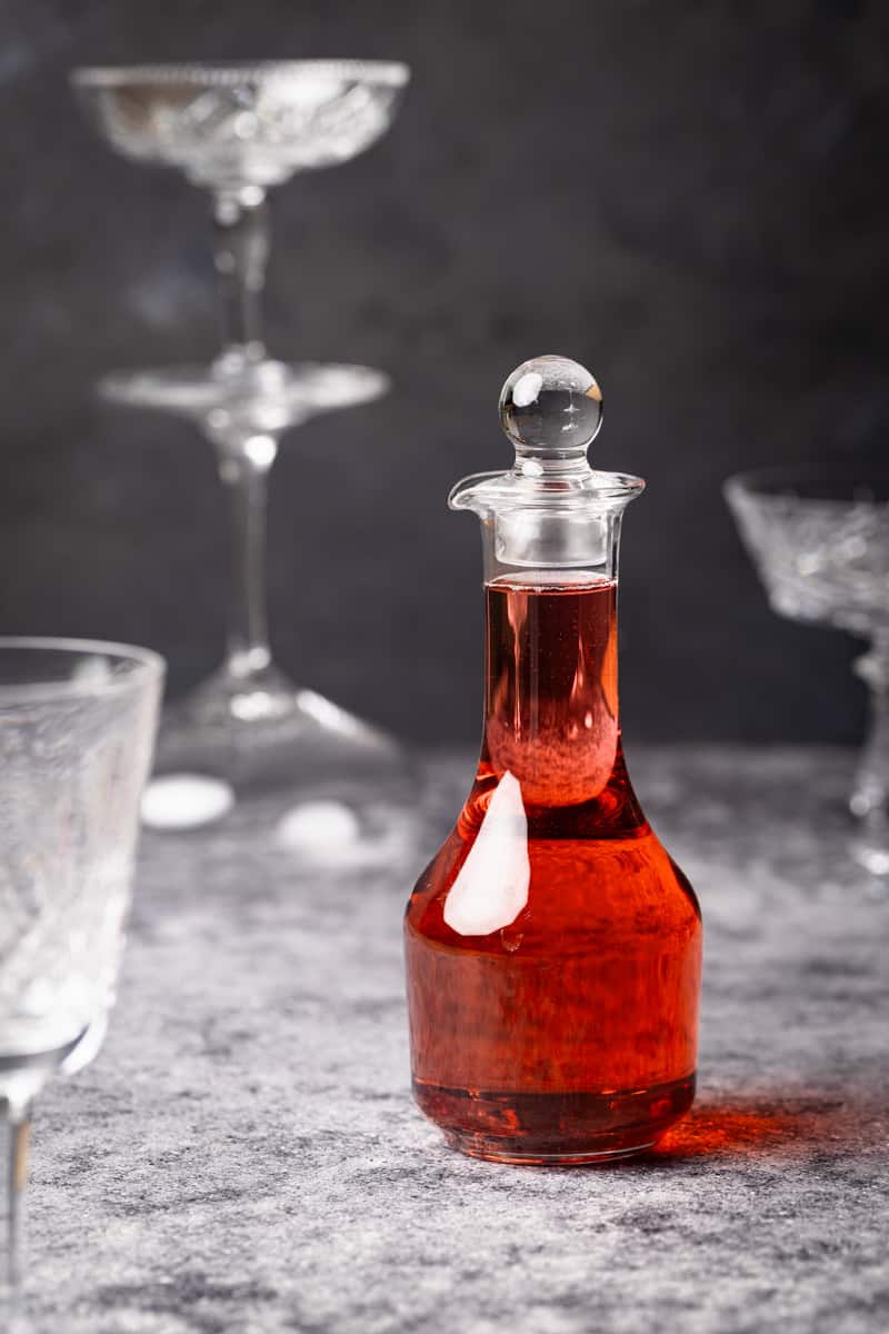 A bottle of homemade Rosé simple syrup next to wine glasses.