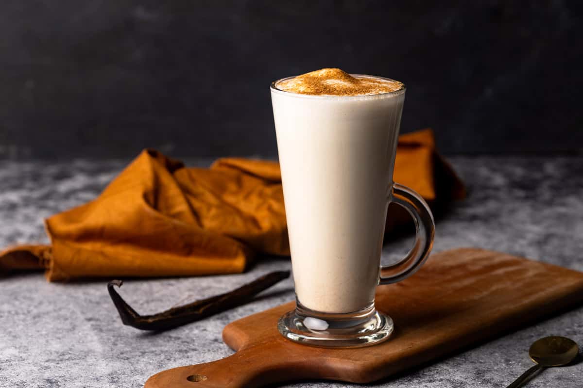 A hot vanilla drink in a glass cup on a wooden board. Moody scene.