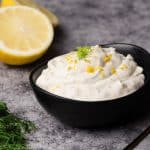 Lemon dill sauce in a black bowl next to lemons and dill.