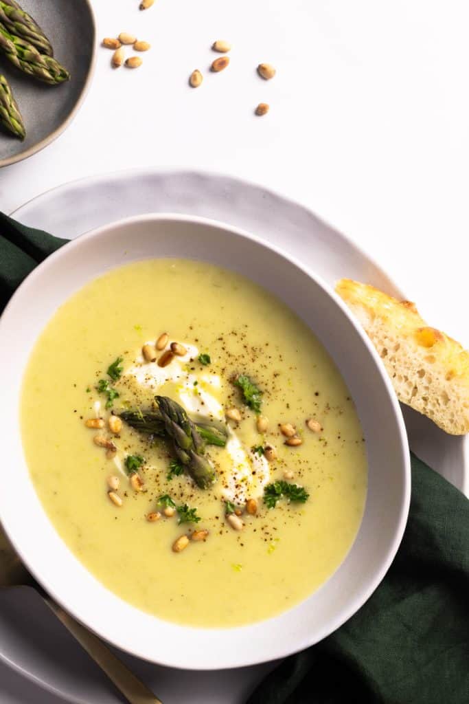 A bowl of asparagus potato soup next to some crusty bread. Flatlay.