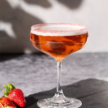 A Rosé margarita cocktail on a shingle slate next to strawberries.