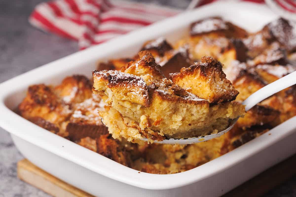 French toast casserole being scooped out of a baking dish.