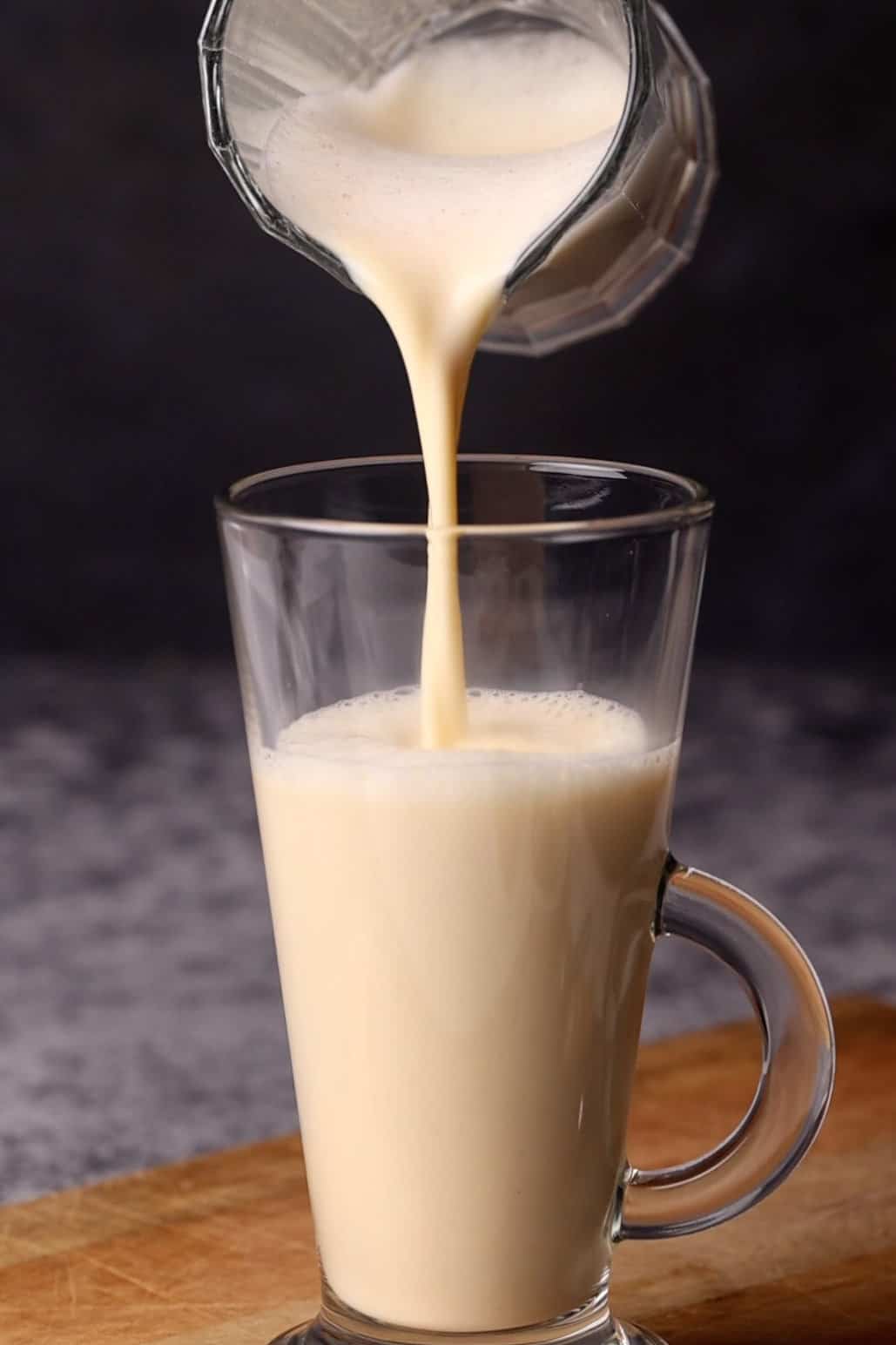 Creamy egg milk being poured into a tall glass cup.