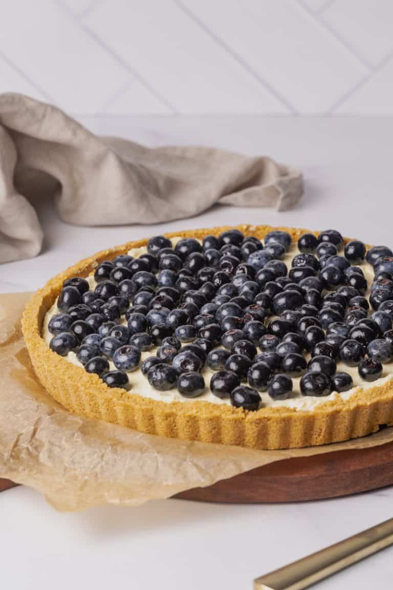 Lemon and blueberry torte on a wooden board next to a linen tea towel.
