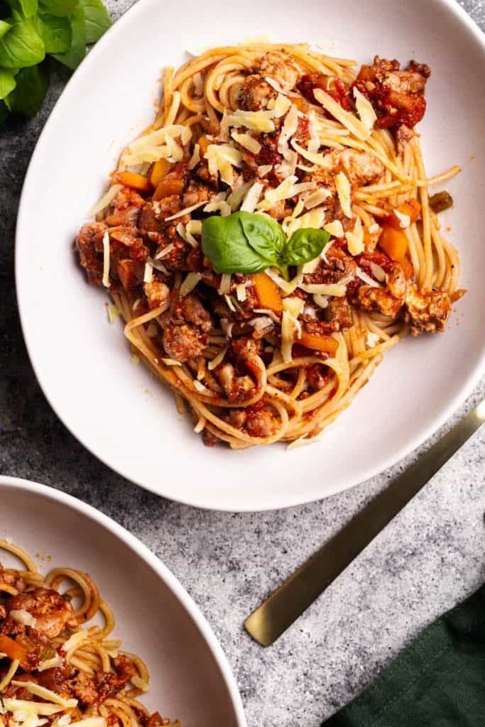 Two white bowls of Ground Chicken Spaghetti Bolognese on a grey background.